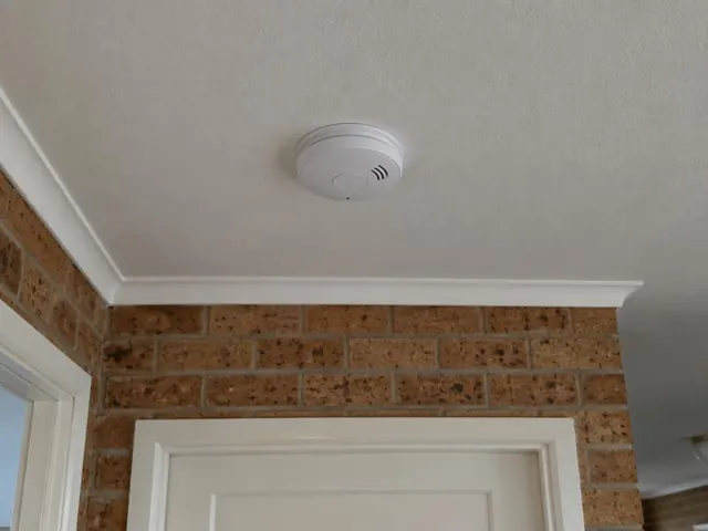 Ceiling-mounted smoke alarm above a brick interior wall and doorway in a home in Elermore Vale